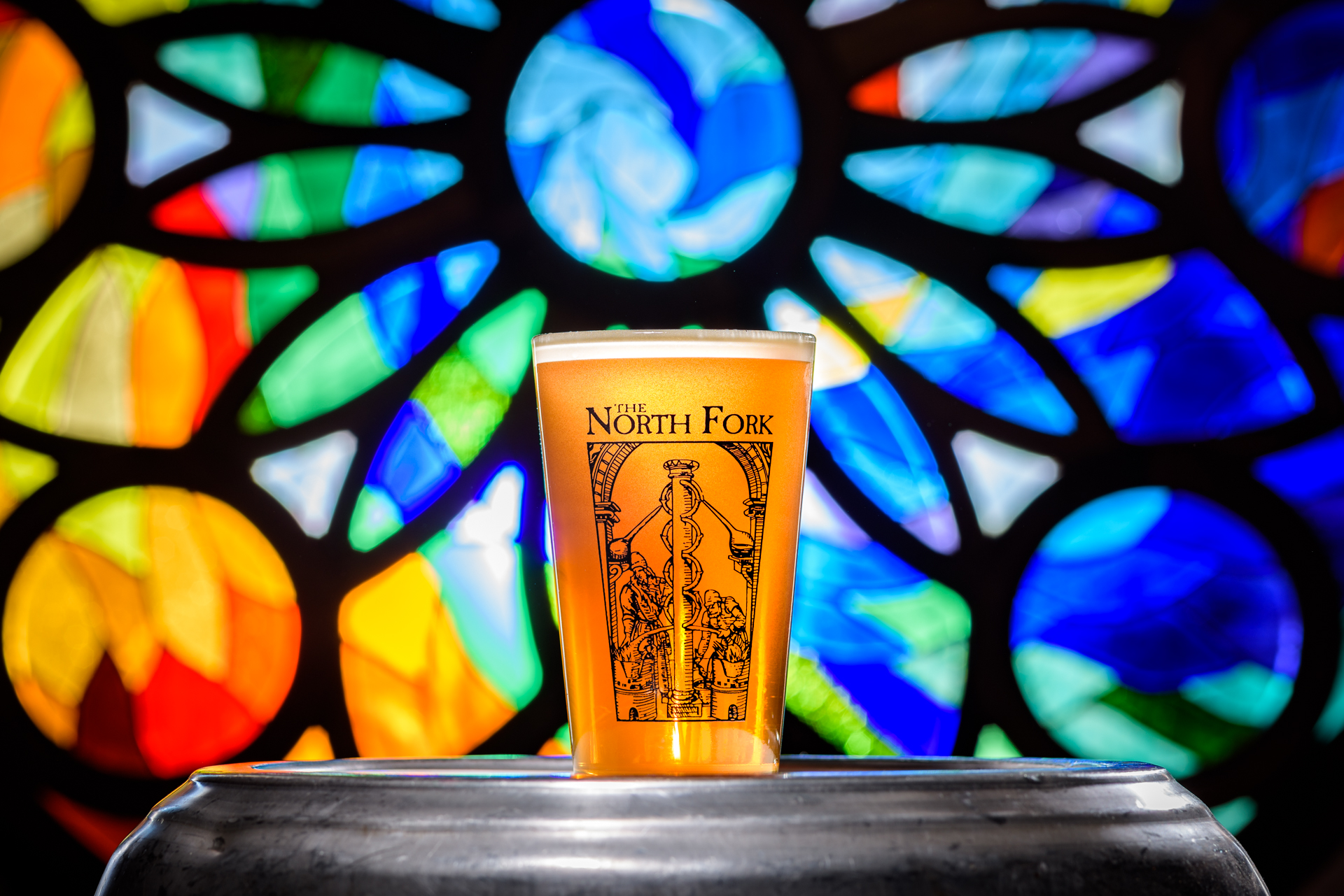 a beer back lit glowing in front of a stained glass window